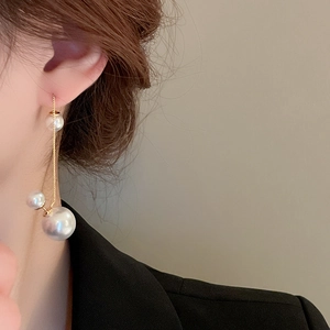 Detail of long pearl tassel earrings with gold-plated chains worn by a model