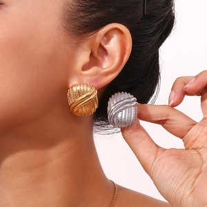 Oval ribbed gold and silver stud earrings shown on ear and held by hand for contrast