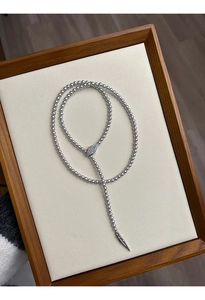 Detail of silver snake-head necklace featuring green stone accents and beaded chain