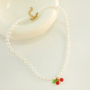 Detail of white pearl necklace featuring a cherry pendant and golden metal clasp