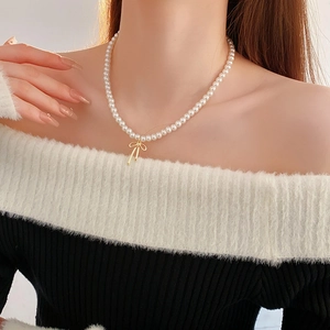 Détail du collier de perles élégant avec un pendentif nœud doré minimaliste sur le décolleté