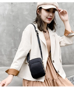 Close-up of black nylon crossbody bag with dual-layer zippers worn over a beige suit