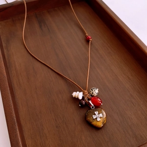 Détail du pendentif cœur en œil de tigre avec perles ethniques sur cordon ciré brun