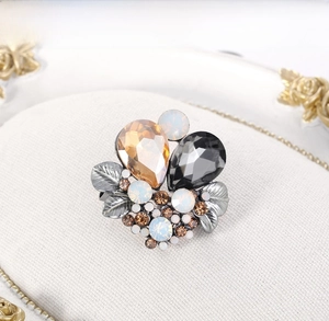 Detail of vintage crystal brooch with metallic leaves on a white oval display stand