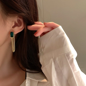 Detail view of emerald green glass earrings with gold tassels on a fashion model