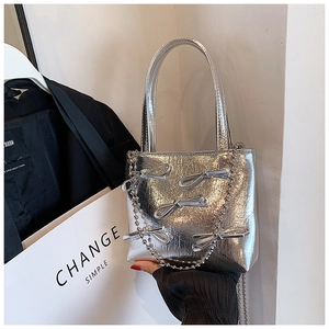 Close-up of silver metallic handbag featuring a bow ornament and a delicate chain strap