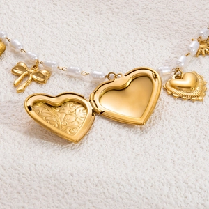 Nahaufnahme der Perlenkette mit goldenem Herzmedaillon, Schleife und Sonnenanhängern