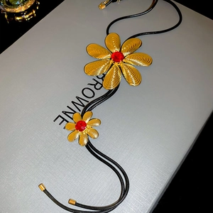 Macro view of gold metal flower pendant with red crystal and textured petals on cord