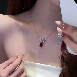 Detail shot of a red teardrop crystal pendant with silver wings on a delicate chain