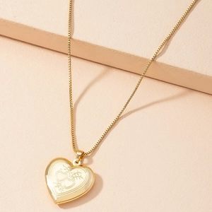 Vintage gold heart locket necklace with floral engraving on a pink background