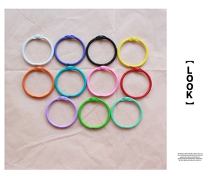 Set of 11 colorful metal loose-leaf binder rings arranged on neutral textured paper