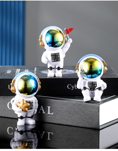 Dettaglio di tre statuine di astronauti in resina bianca con stelle dorate su dei libri