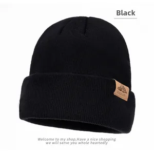 Close-up of black knitted beanie with a brown leather mountain logo patch on the side