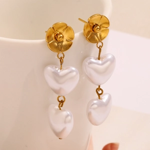 Detail von goldenen Blumenohrringen mit doppelten Herzperlen an einer weißen Keramiktasse