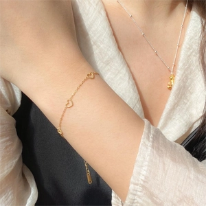 Close-up of a delicate gold heart bracelet with three hollow charms on a wrist
