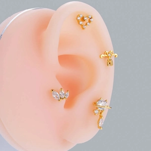 Close-up of golden stud earrings with zircons in heart and butterfly shapes on ear model