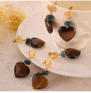 Close-up of heart-shaped tiger eye earrings with green beads on ceramic tray