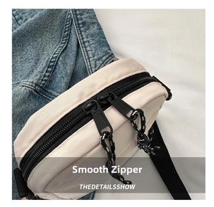 Detail view of smooth double zippers with woven cords on beige oxford crossbody bag