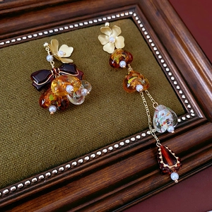 Detailed close-up of asymmetric amber drop earrings with golden chains and pearls