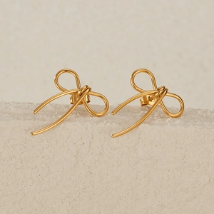 Detailed view of elegant gold bow stud earrings displayed on a textured stone base