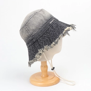 Détail d'un bob en jean délavé avec bords effilochés, logo métal et cordon coupe-vent