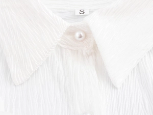 Detail of white pleated texture fabric with elegant pearl button and shirt collar