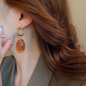 Close-up of a model wearing golden C-shape earrings with amber resin pendant drops
