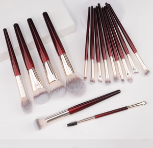 Top view of 15 professional synthetic makeup brushes with wine red handles on stone