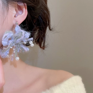 Detail shot of purple knit flower earring with white pearls on a model ear