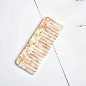 Macro detail of pink marble acetate wide tooth comb on minimalist book page background
