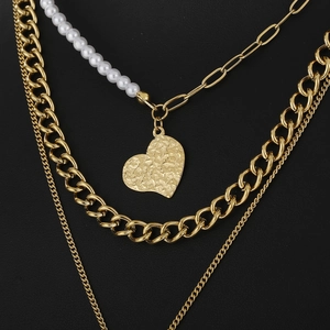 Layered gold necklace featuring pearls and a hammered heart pendant on a black background