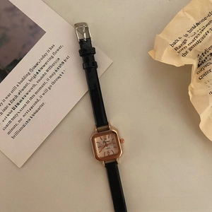 Close-up of vintage square gold watch with black leather strap and quartz dial