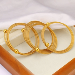 Dettaglio di tre bracciali a filo attorcigliato oro con estremità sferiche su velluto