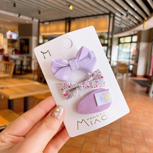 Detailed shot of purple fabric bow clips and floral embroidery on white card packaging