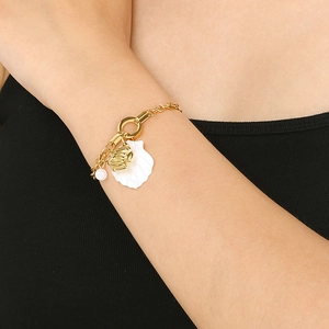 Close-up of golden titanium steel bracelet with white shell and fish charms on wrist