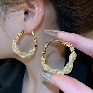 Close-up of large golden twisted hoop earrings featuring sparkling pave-set cubic zirconia