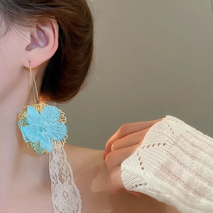 Gros plan d'une boucle d'oreille fleur bleue avec cadre doré sur mannequin de mode