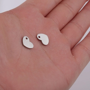 Close-up of small silver stainless steel heart charms held in hand for scale