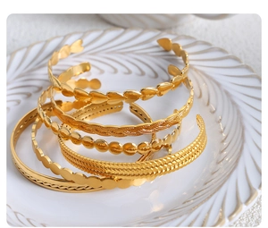 Macro view of five assorted 18k gold plated stainless steel bangles in a white ceramic tray