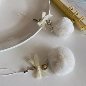 Detail of white plush pompom charm with silk bow and silver star heart pendants