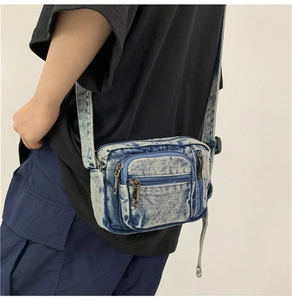 Detail view of washed denim crossbody bag featuring metal zippers and multiple pockets