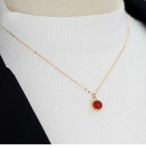Close-up of gold titanium necklace with round red agate pendant on a white sweater