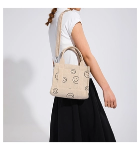 Vista laterale dettagliata della borsa tote in velluto beige con stampa smiley nera