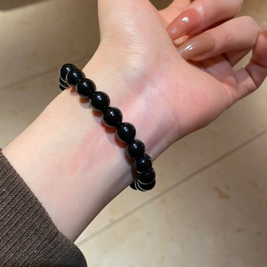 Close-up of polished black obsidian beaded bracelet worn on wrist with brown knit sleeve