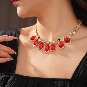 Close-up of vintage gold necklace with red teardrop gemstones and bow detailing on a model