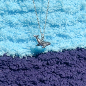 Detailed view of 925 sterling silver whale pendant on a fine chain over blue fabric