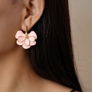 Detail of pink floral earrings with gold edges worn by a model in soft lighting
