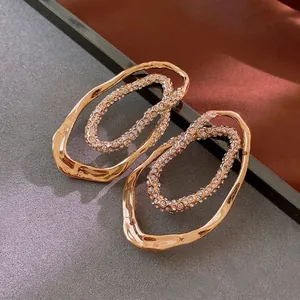 Gold plated irregular oval earrings with pavé crystals on artistic textured background