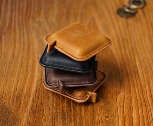 Vertical stack of vintage leather measuring tapes in four colors on wood background
