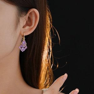 Close-up of model wearing geometric rhombus gold earrings with purple crystal pendants